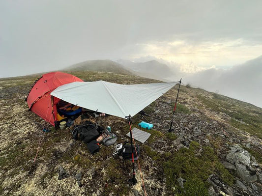 Camping setup with a red tent and tarp on a mountain landscape