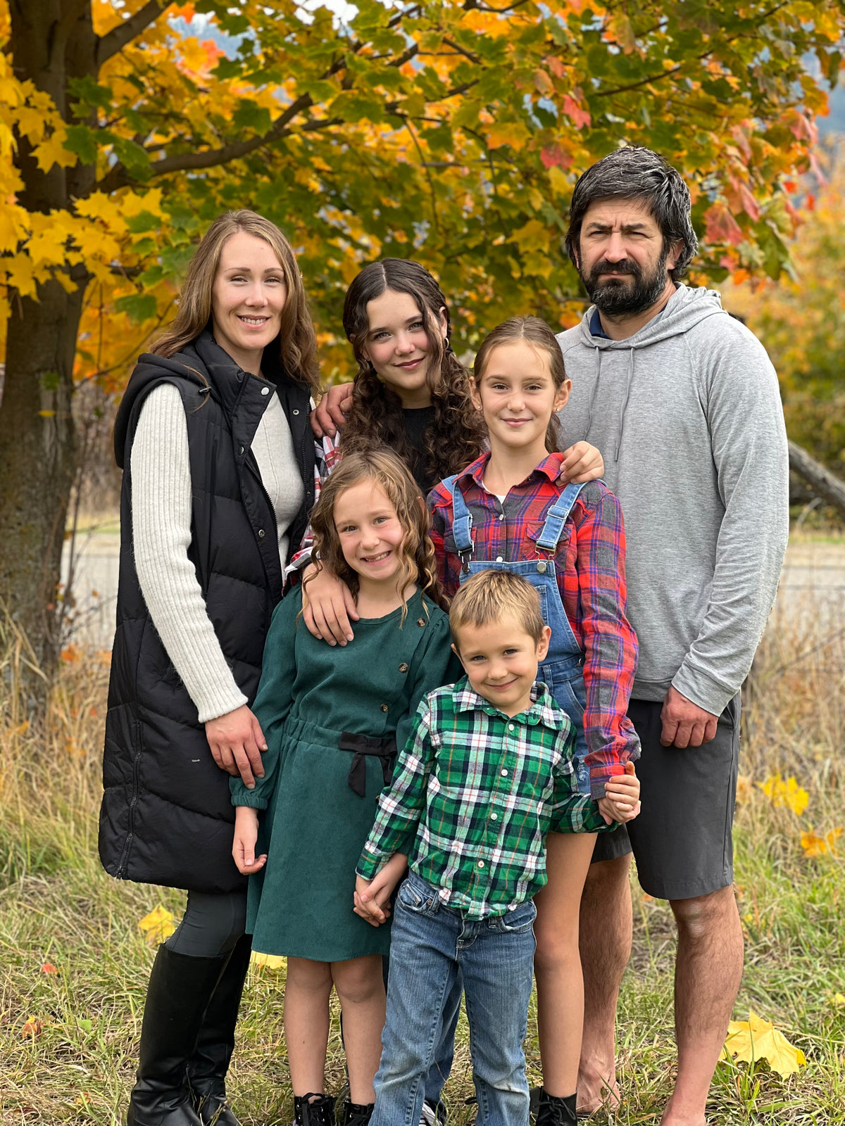 Family of five standing outdoors with autumn foliage in the background