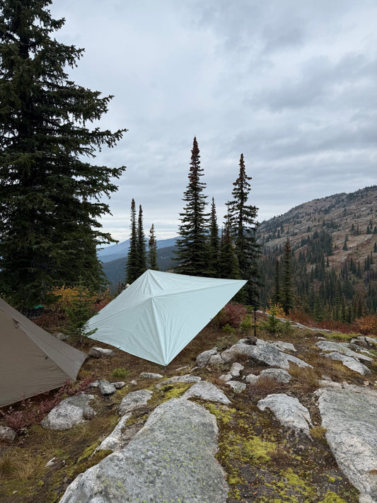 Tent pitched on a rocky mountain terrain with trees and sky.
